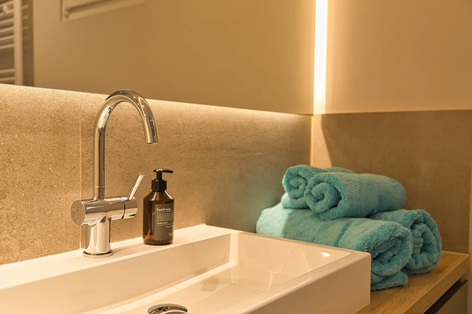 Waschtisch mit edler Armatur und gerollten Handtüchern.