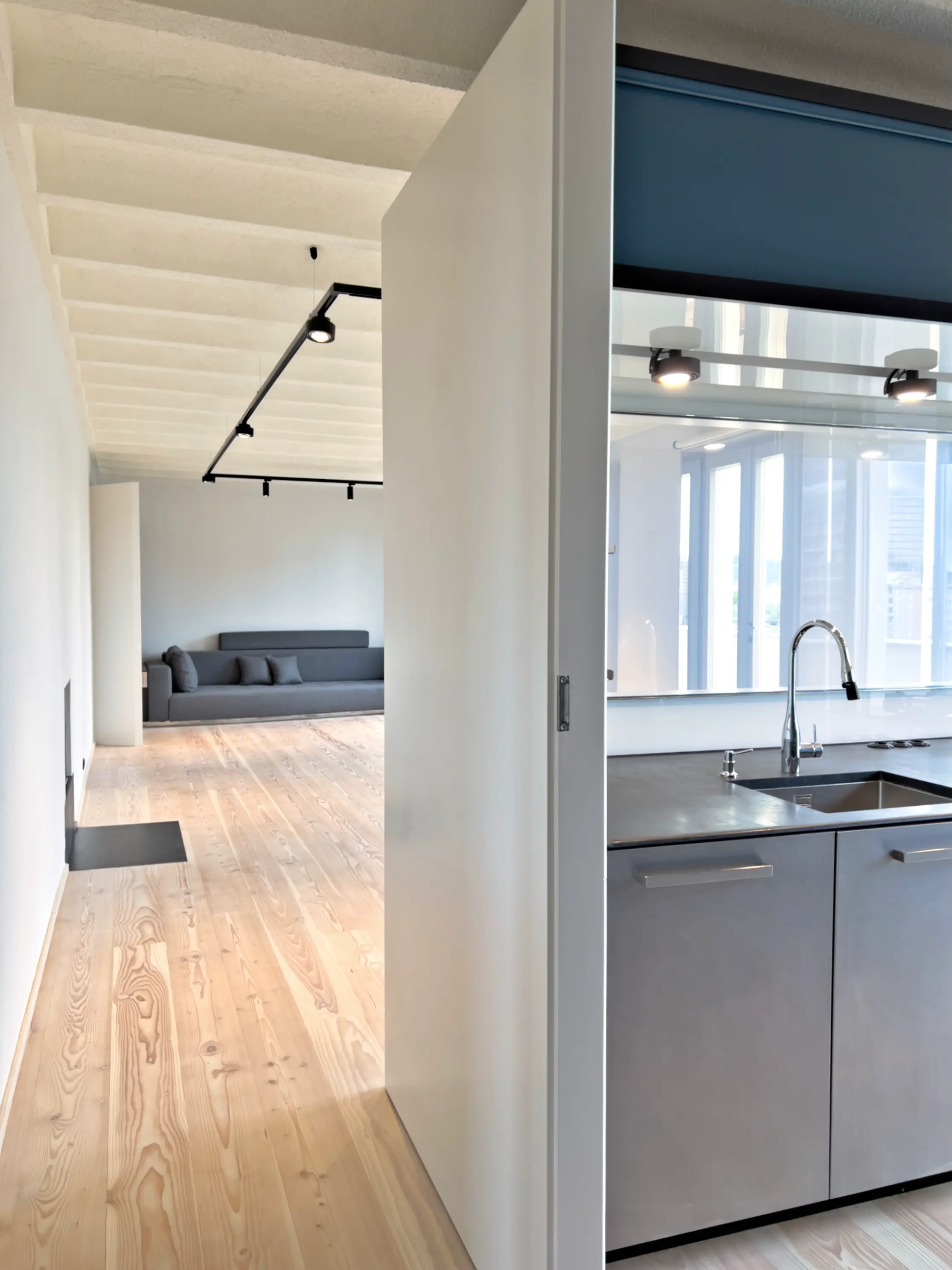 Übergang von Wohnraum zur Küche mit schwarzer Schiebetür und hellem Holzfußboden.