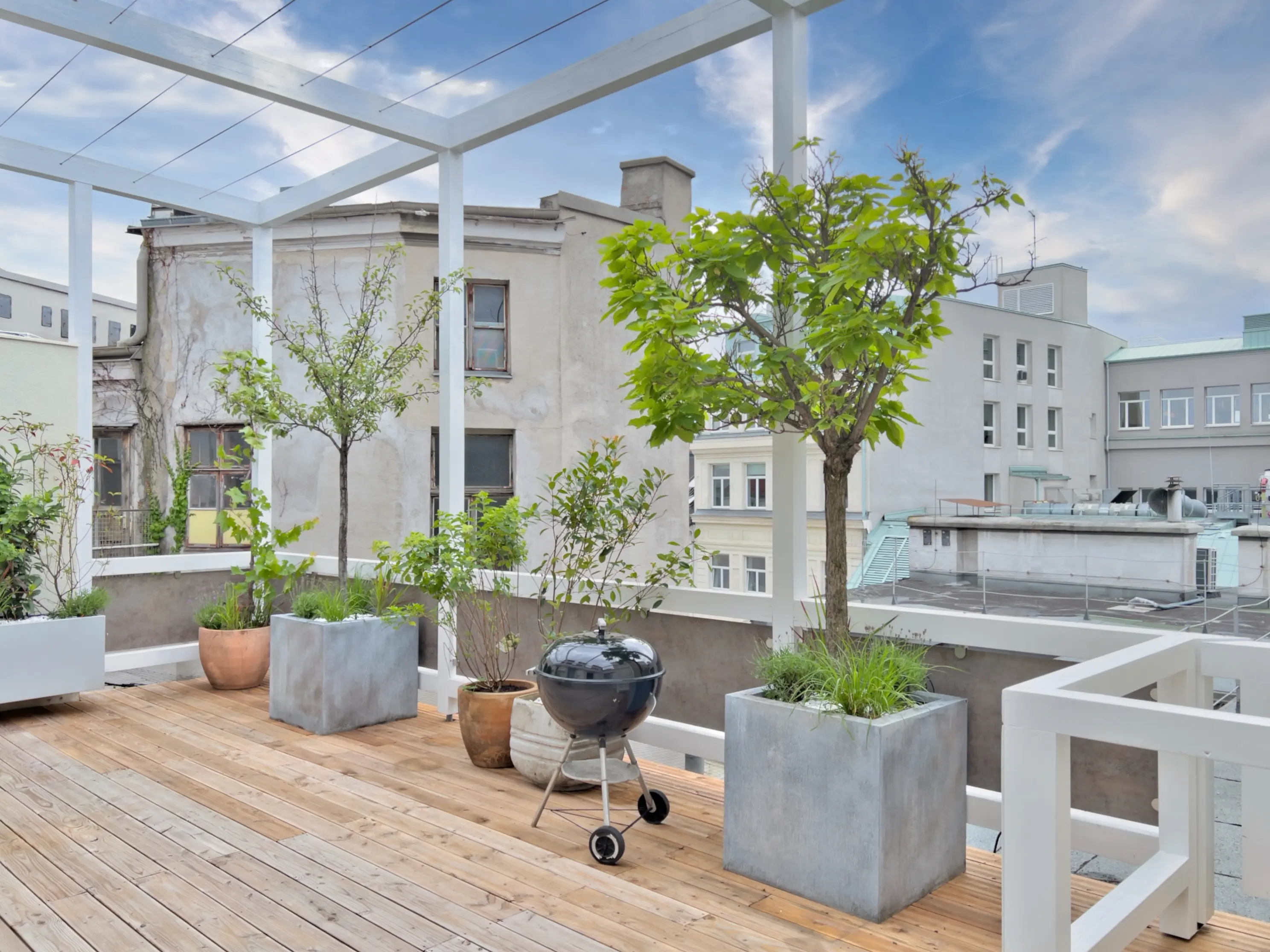 Begrünte Dachterrasse mit Pflanzkübeln, Holzboden und Sitzgelegenheiten.