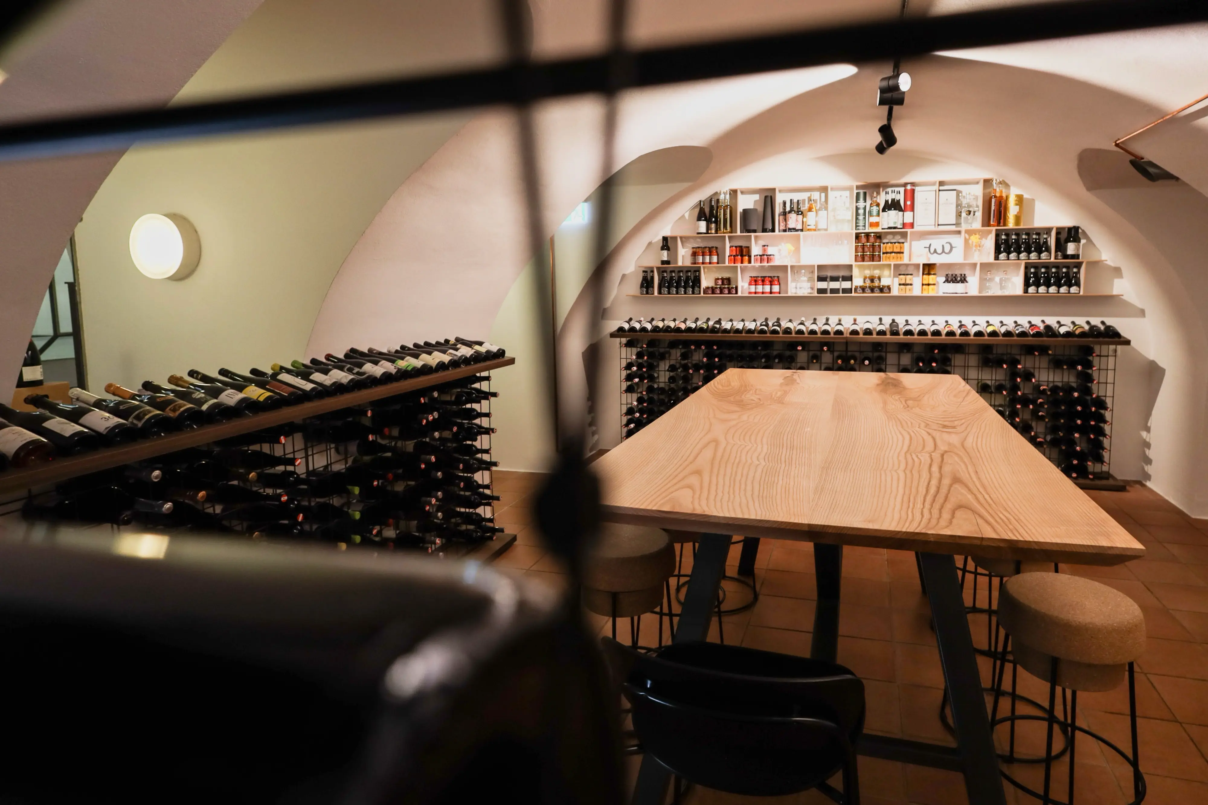Holztisch mit Blick auf die Weinregale – Warme, einladende Sitzecke inmitten eines stilvollen Weinkellers mit einer großen Auswahl an edlen Tropfen.